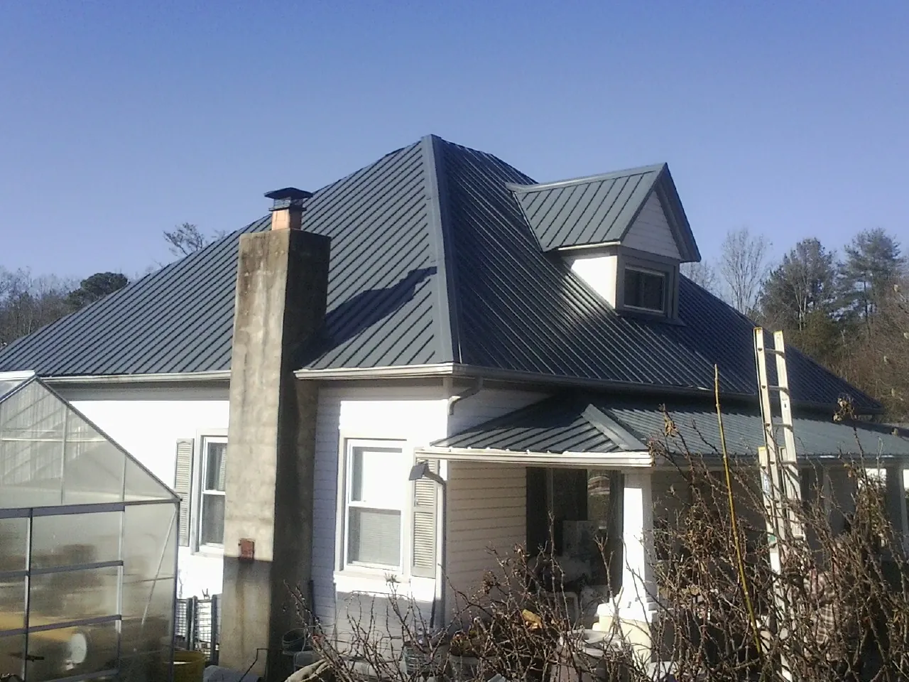 Dark blue standing seam metal roof on a white farmhouse with dormer — Slate & Tile Roof Repair by Roofing Brothers in Saranac