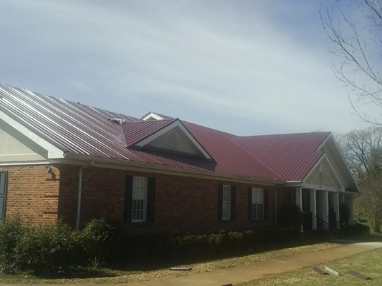 Red metal roof with gabled entries on a long brick building, from a Hail Damage Roof Repair job in Saranac