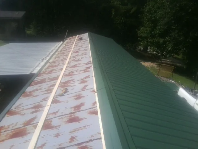 Old rusted panels beside newly installed green metal roofing — Wind Damage Roof Repair by Roofing Brothers in Saranac