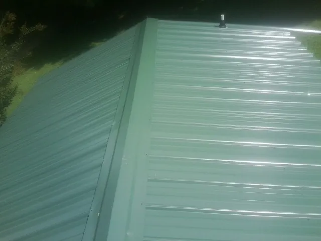 New green metal panels meeting at the ridge of a roof — Flat Roof Repair work by our crew in Saranac