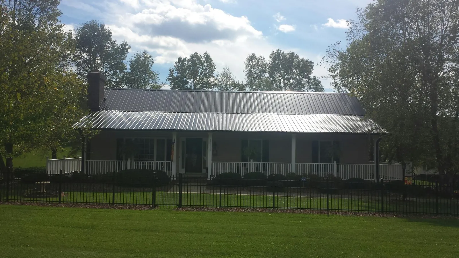 Gray metal roof on a brick ranch with a full width front porch — Gutter Guard Installation work by our crew in Saranac