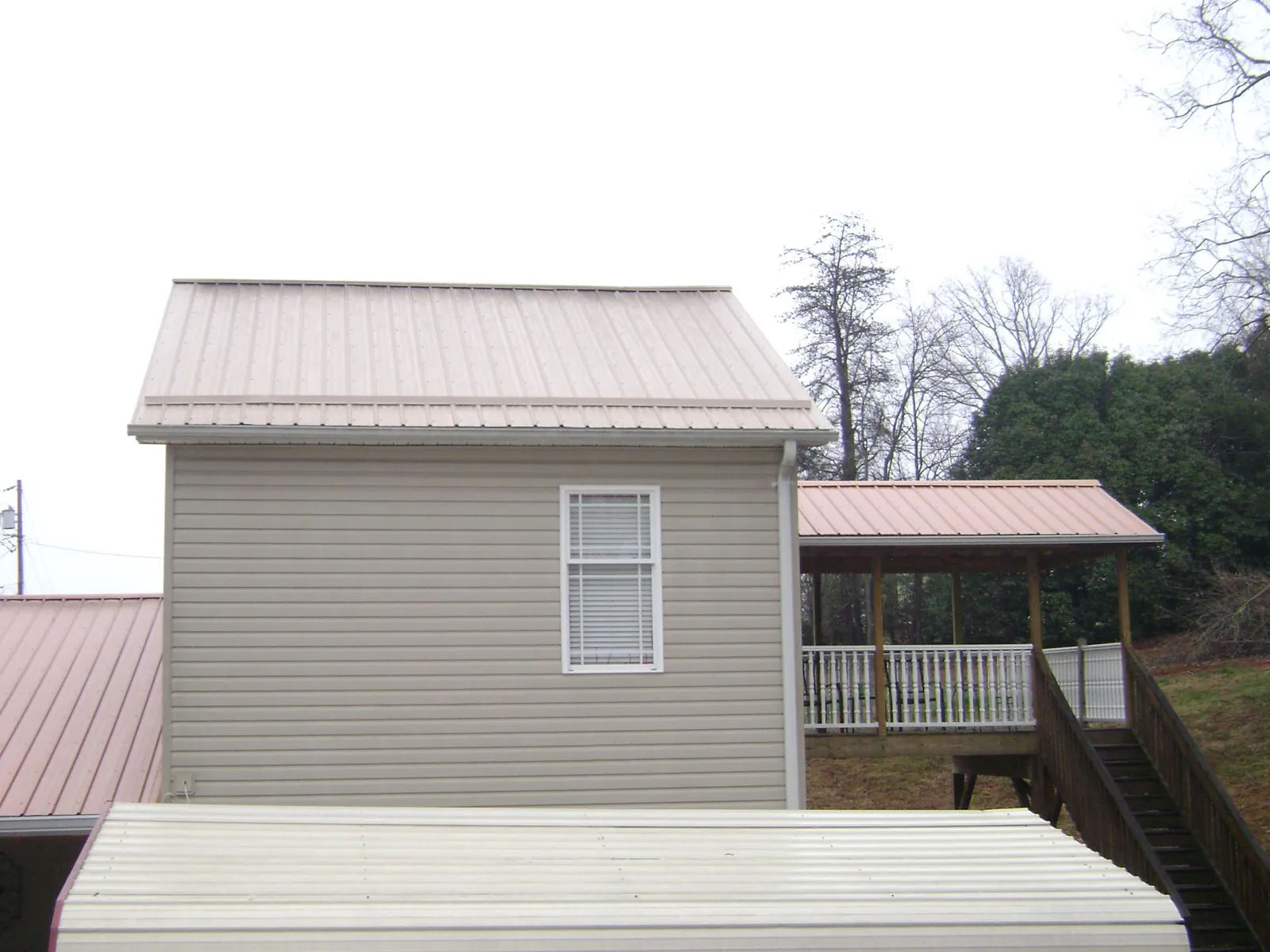 Tan metal roofs on a two story addition and attached porch, from a Roof Replacement job in Saranac