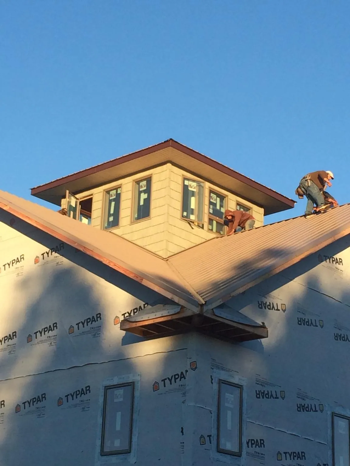 Roofers working around a rooftop cupola on a new metal roof at sunset — Roof Waterproofing in Saranac by Roofing Brothers